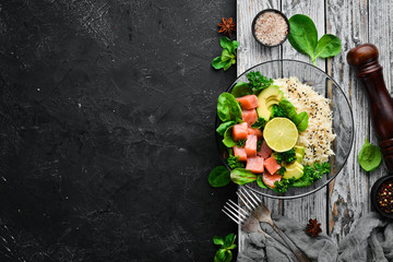 Rice with salmon, avocado and spinach. In a black plate on a wooden background Top view. Free space...