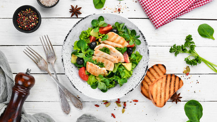 Salad with chicken fillet, olives, tomatoes and avocados in a plate on a wooden background Top view. Free space for your text. Flat lay