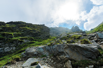 hiking uphill rocky slopes of fagaras mountains. hard path among big and sharp boulders. sunny summer weather with cloudy sky