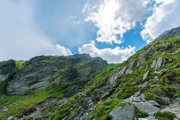 Fototapeta na wymiar hiking uphill rocky slopes of fagaras mountains. hard path among big and sharp boulders. sunny summer weather with cloudy sky