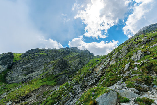 hiking uphill rocky slopes of fagaras mountains. hard path among big and sharp boulders. sunny summer weather with cloudy sky