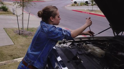 High angle of a female replacing a dipstick after checking oil levels in her driveway, 23.98 fps.