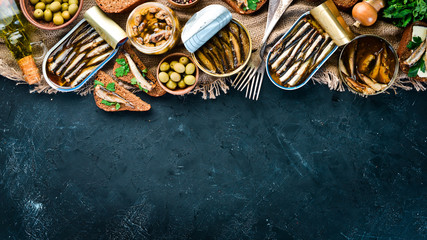 Assortment of sprats in oil. Smoked fish On a black background. top view. Free copy space. - obrazy, fototapety, plakaty