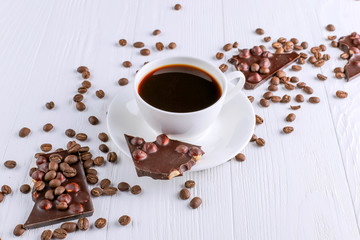 Scattered coffee grains, a cup and black chocolate on a white wooden table. Copy space.