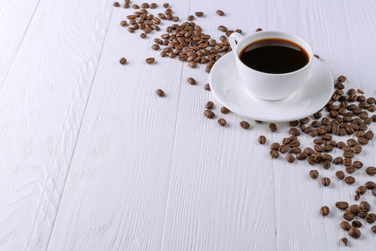 Scattered coffee grains, a cup and black chocolate on a white wooden table. Copy space.