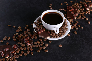 Obraz na płótnie Canvas Scattered coffee grains, a cup and black chocolate on a black stone table. Copy space.