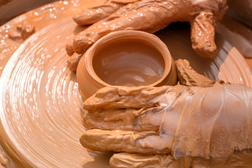 Hands of a street potter make a clay pot on a potter's wheel. Close-up