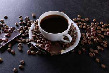 Obraz na płótnie Canvas Scattered coffee grains, a cup and black chocolate on a black stone table. Copy space.