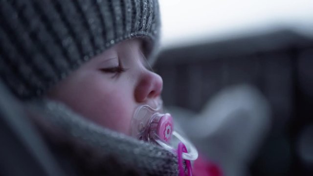 Tight closeup shot of a Caucasian baby wearing a grey beanie with a pacifier in the mouth on a cold day