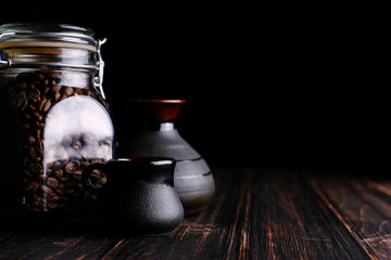 A can of coffee, a cup and a turk on a wooden table, on a black background.