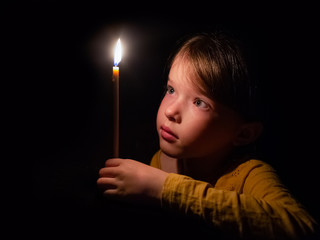 little girl prays and looks at a burning candle in the dark