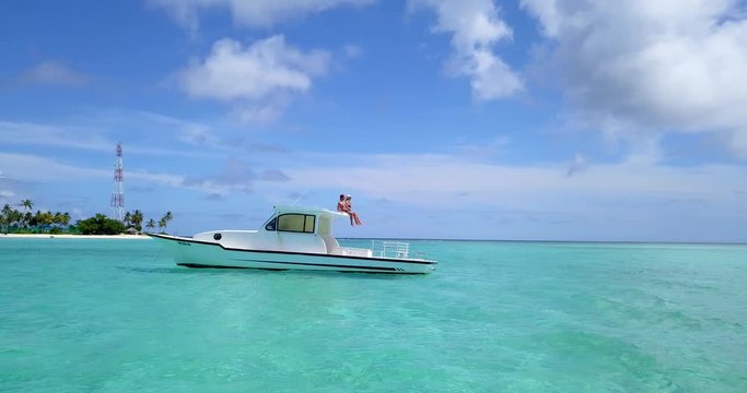 Couple sit on white boat in Hanimaadhoo island bay, aerial pan to left 4k