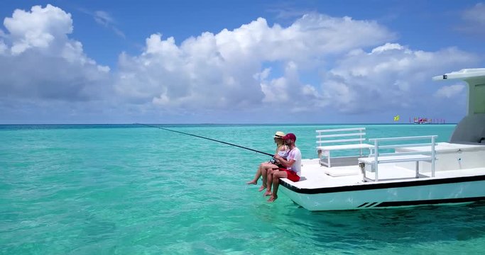 Young man and woman sitting on speedboat fishing in crystal clear waters of Maldives, pan shot 4k