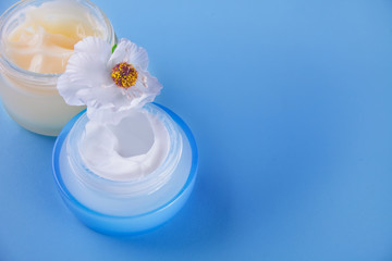 Fototapeta na wymiar glass jars of beauty cream with white flower on the blue background. Top view. Copy space.