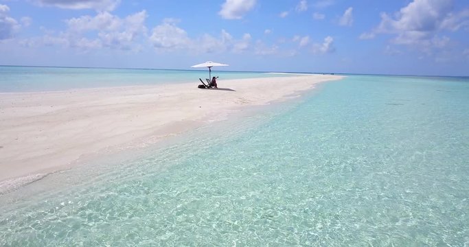Woman relaxing under beach umbrella and takes selfies on pristine Maldives tropical sandbar