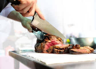 Chef with knife and cutting tasty grilled steak, Chef preparing food, meal, in the kitchen chef at...