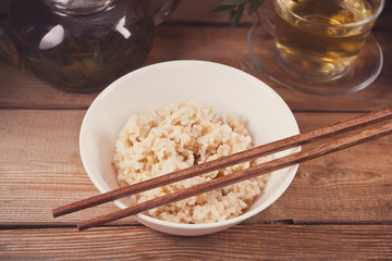 Cooked brown rice in white bowl with chopsticks on the wooden background.