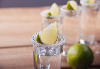 Tequila shot with lime and sea salt on old wooden table, selective focus
