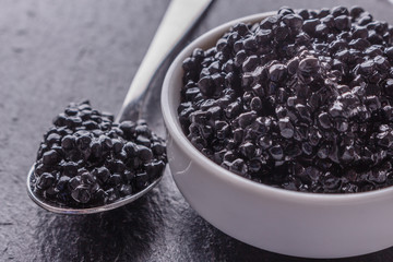 Fototapeta na wymiar black caviar in a bowl on a dark stone background