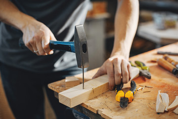 A man carves a tree. The carpenter works with hammer in a studio. An engineer provides a tree shape