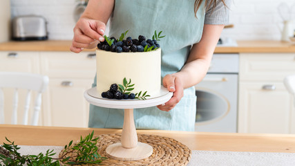 Confectioner decorating wedding cake with berries. Close up. White cake with cream cheese and fresh blueberries and blackberries. Copy space. Confectionery concept
