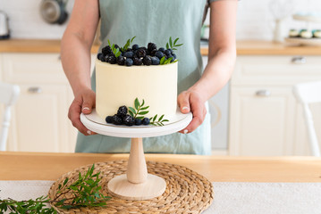 Confectioner holding wedding cake with berries. Close up. White cake with cream cheese and fresh blueberries and blackberries. Copy space. Confectionery concept