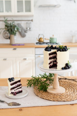 White cake with cream cheese, fresh blueberries and blackberries and piece of cake on the kitchen table. Confectionery, bakery concept. Close up. Copy space