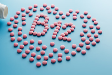 Pink tablets in the form of B12 in the heart on a blue background, spilled from a white can.