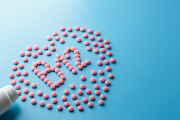 Pink pills in the shape of the letter B12 on a blue background, spilled out of a white can.
