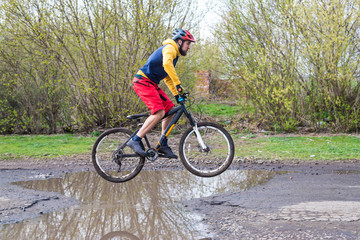 Naklejka premium A cyclist in red shorts and a yellow jacket riding a bicycle on the rear wheel through a puddle.