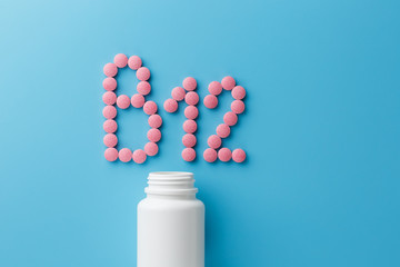 Pink pills in the shape of the letter B12 on a blue background, spilled out of a white can.