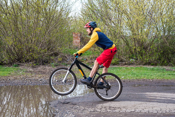 Fototapeta na wymiar A cyclist in red shorts and a yellow jacket riding a bicycle on the rear wheel through a puddle.