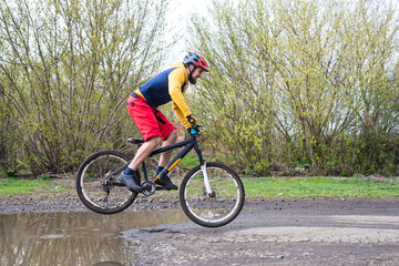 A cyclist in red shorts and a yellow jacket riding a bicycle along a street with puddles.