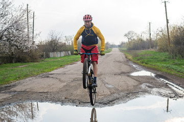 A cyclist in red shorts and a yellow jacket riding a bicycle along a street with puddles.