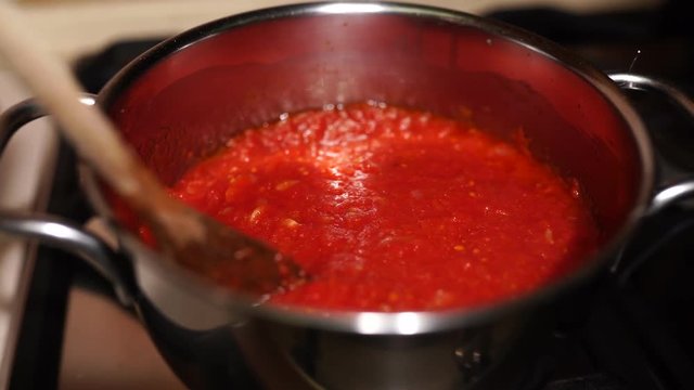 Delicious tomato sauce with onion and garlic boiling in metalic pan. Woman hand stirring slowly sauce with wooden spoon. Italian cuisine