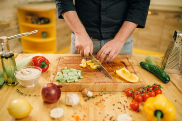 Chef hands with knife cuts yellow pepper closeup