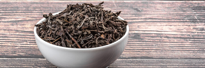 Dried tea is poured into a ceramic cup on a wooden plank table.