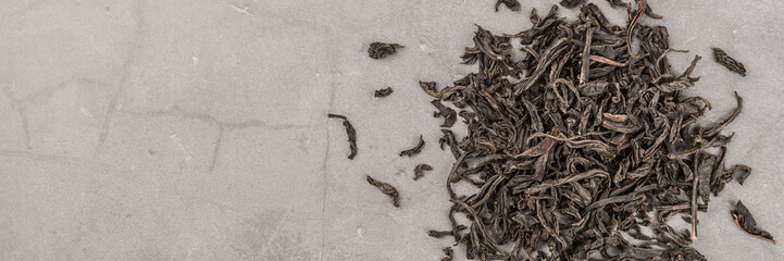 Dried tea is poured scattered on a grey textured background.