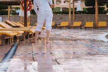 A working man collects rubbish on the territory of the hotel and washes the floor near pool