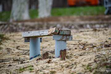Small wooden old bench, with peeling paint in the sand on the beach among nature and trees