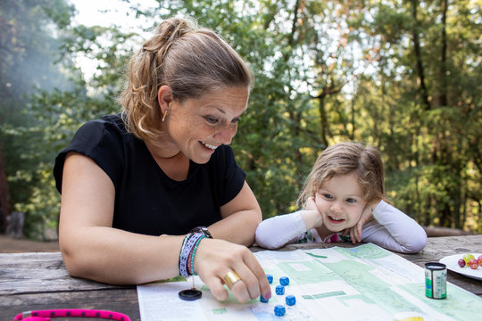A mother and daughter playing a dice game together at a outdoor table.