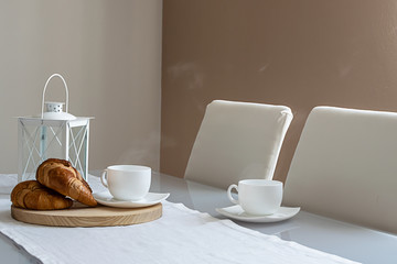 Minimalistic style interior. Tasty breakfast with fresh croissants and hot steaming coffee.