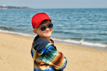 Portrait of a boy on a walk by the sea on a spring day . Boy in red cap and sunglasses