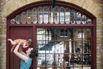 Fototapeta na wymiar Mother holding daughter in the air in front of shop window. 