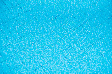 Water ripples on blue tiled swimming pool background. View from above.