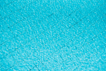 Water ripples on blue tiled swimming pool background. View from above.