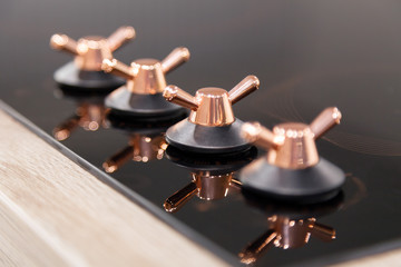Obraz premium Closeup of the copper knob switch plates are reflected in the black shiny electric or gas hob for the kitchen. Concept modern household appliances in vintage style