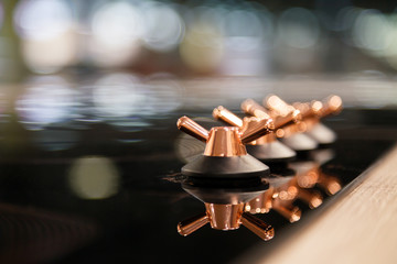 Closeup of the copper knob switch plates are reflected in the black shiny electric or gas hob for...