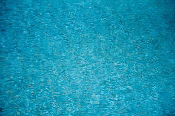 Fototapeta na wymiar Water ripples on blue tiled swimming pool background. View from above.