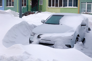 Сar covered with snow stands in parking lot of residential building in winter. Сoncept of bad weather, snowfall, harsh weather conditions, frost, blizzard, car engine did not start